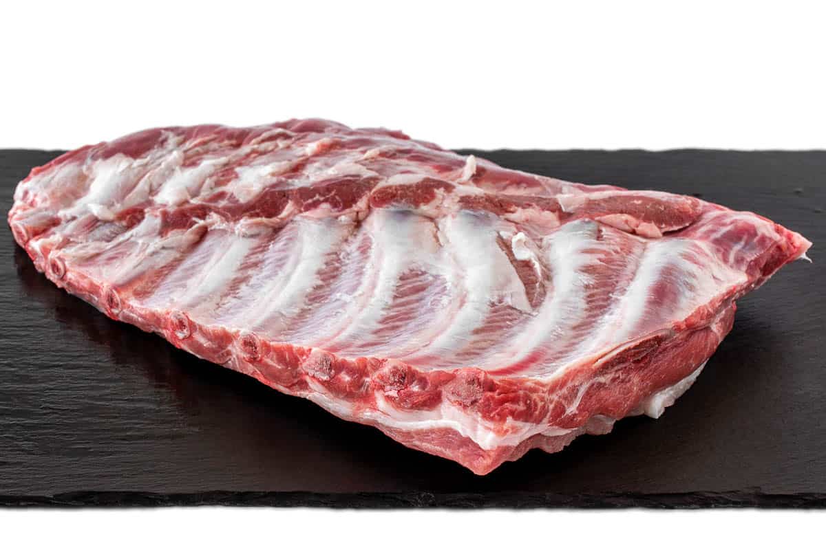 Whole raw pork ribs isolated on dark, black, stone board.