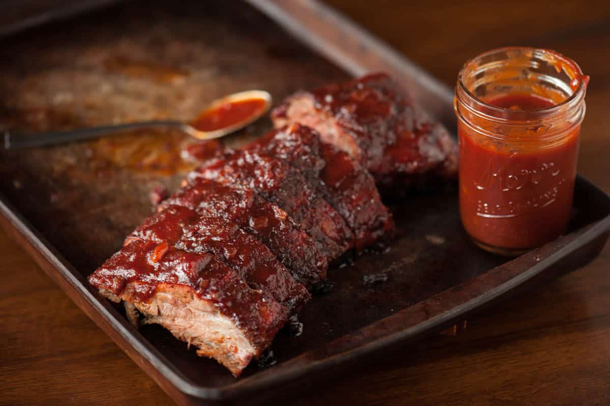 cut baby back ribs with mason jar of barbecue sauce