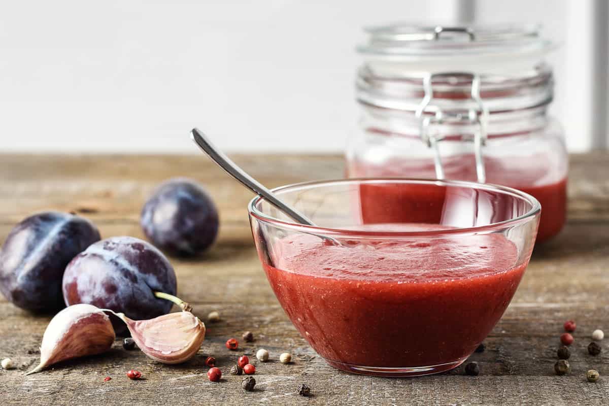 Plum sauce, tkemali in a glass bowl and fresh blue plums on a wooden table.