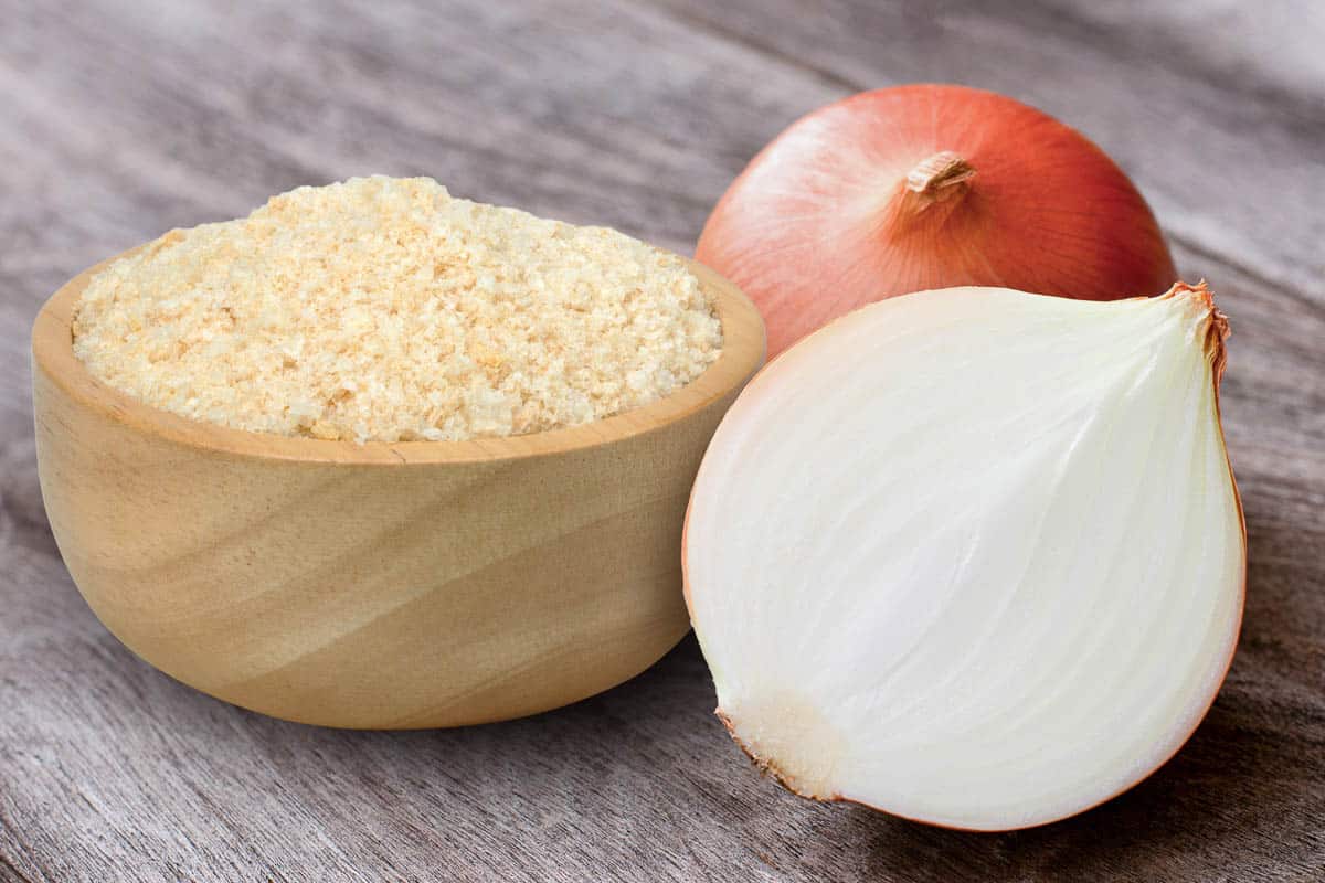 Ground onion or onion powder in wooden bowl and fresh onion with half sliced.