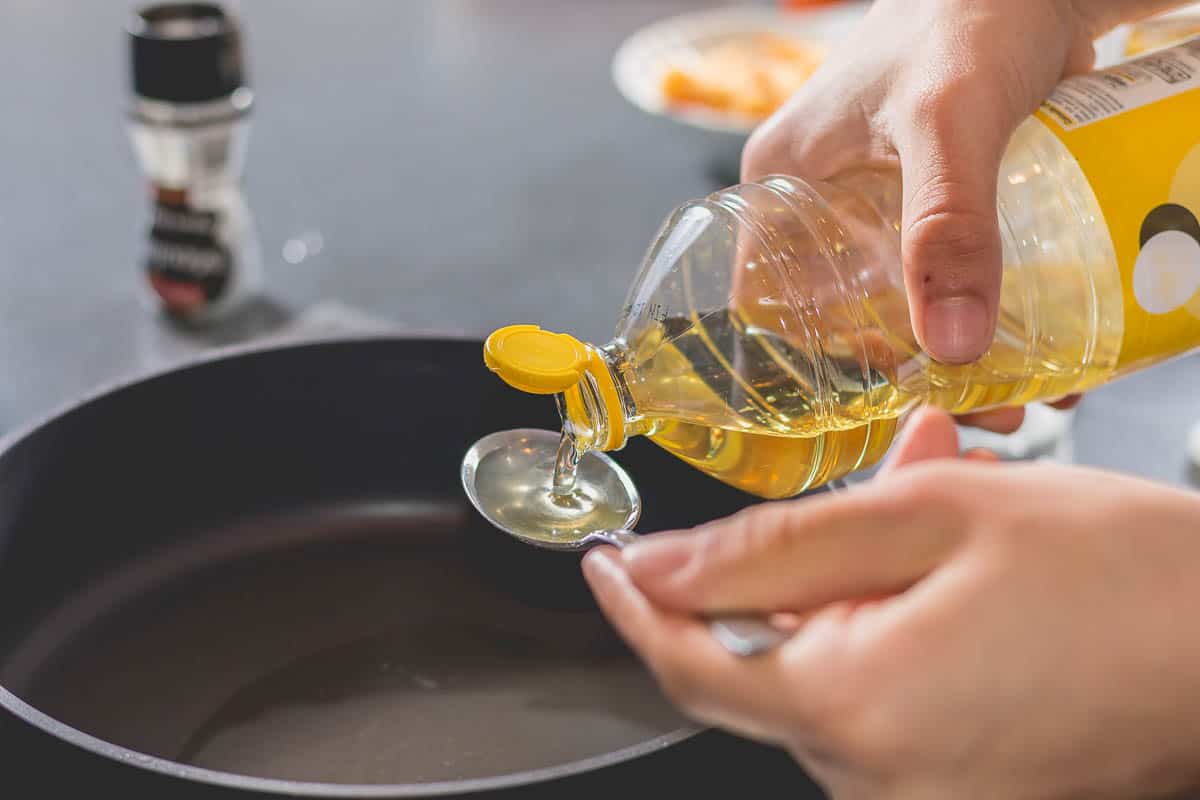 Cook pouring oil into a hot black saucepan.