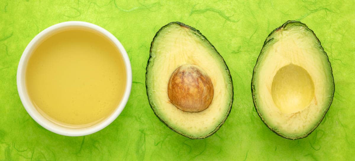 avocado oil in small white dish next to avocado cut in half.