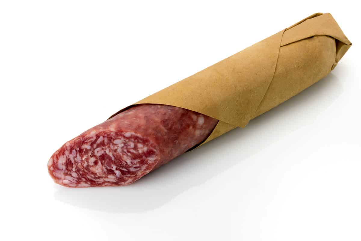 Italian country salami, whole sausage cut and wrapped in butcher paper isolated on white.