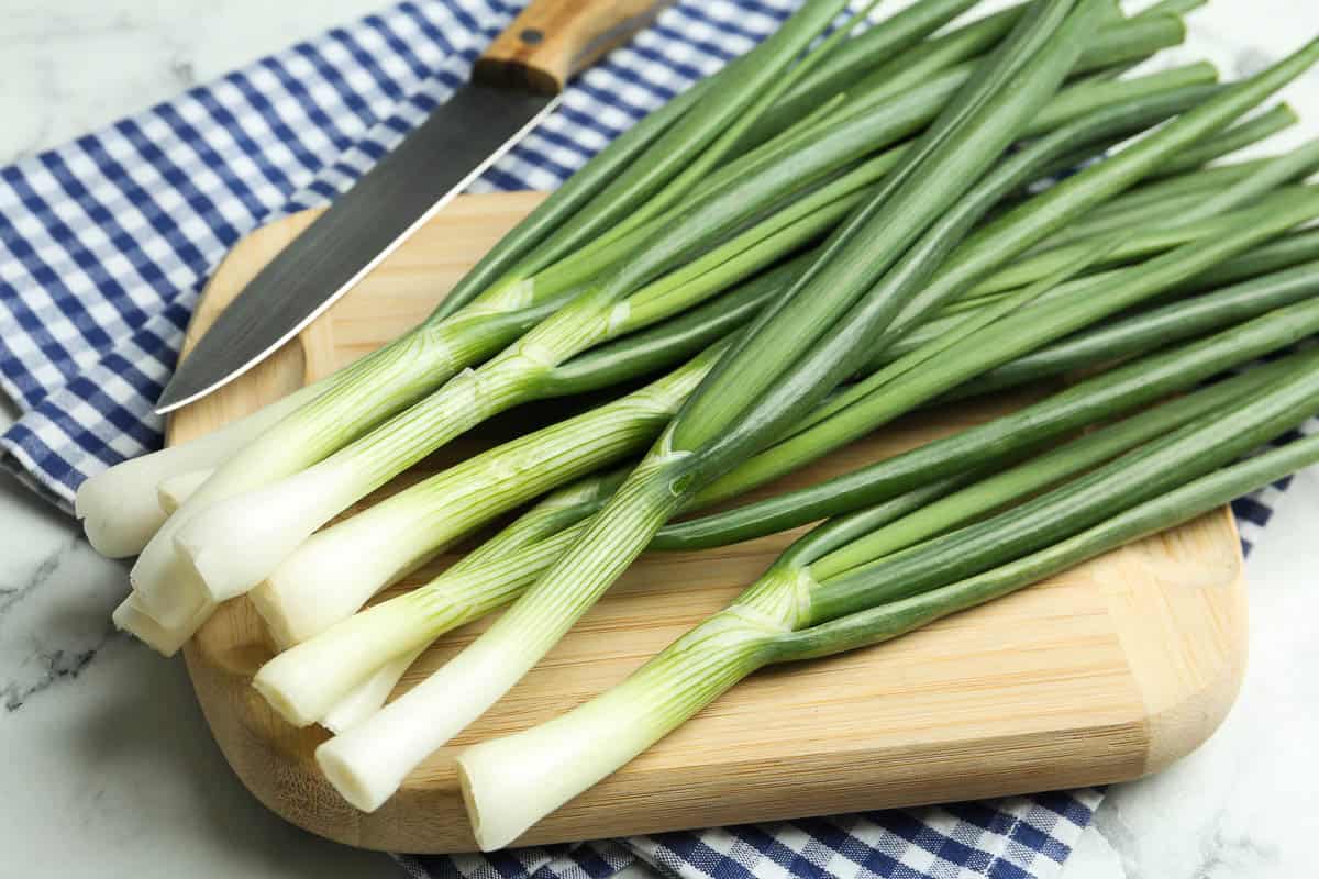 Fresh green spring onions on wooden board, closeup.