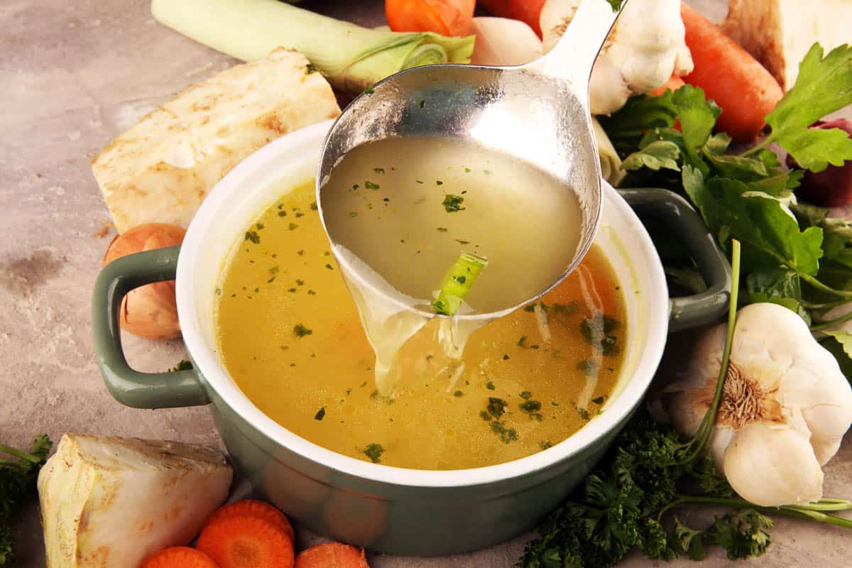 Broth with carrots, onions various fresh vegetables in a pot - colorful fresh clear spring soup.