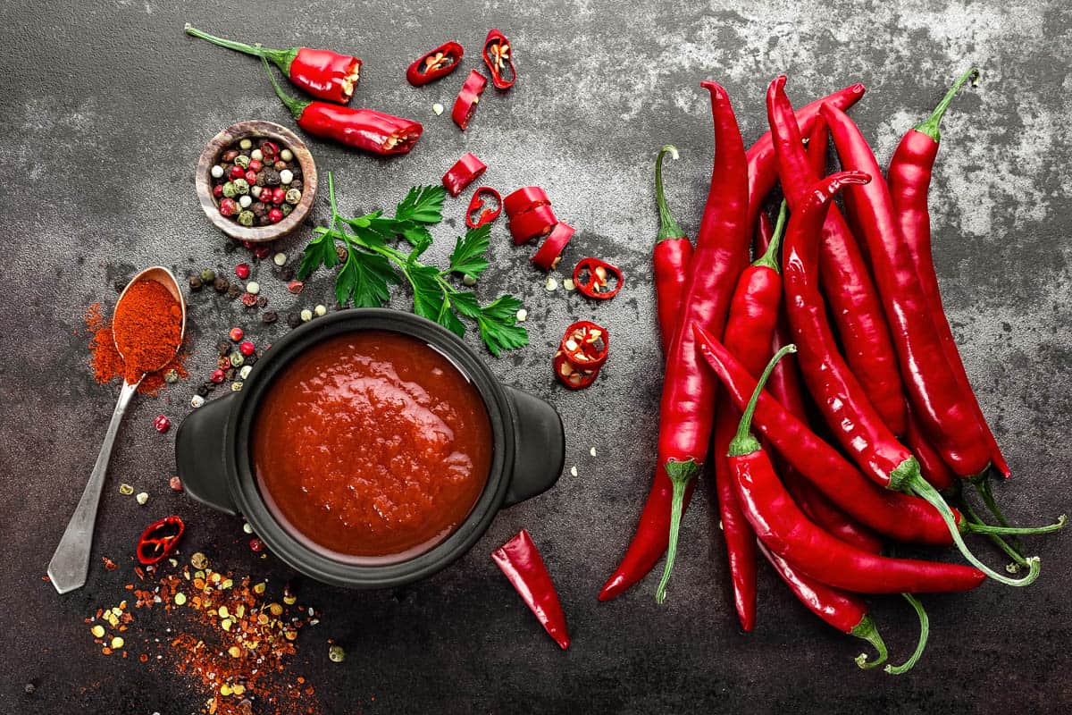 spicy chili sauce, ketchup, red chiles on grey background.