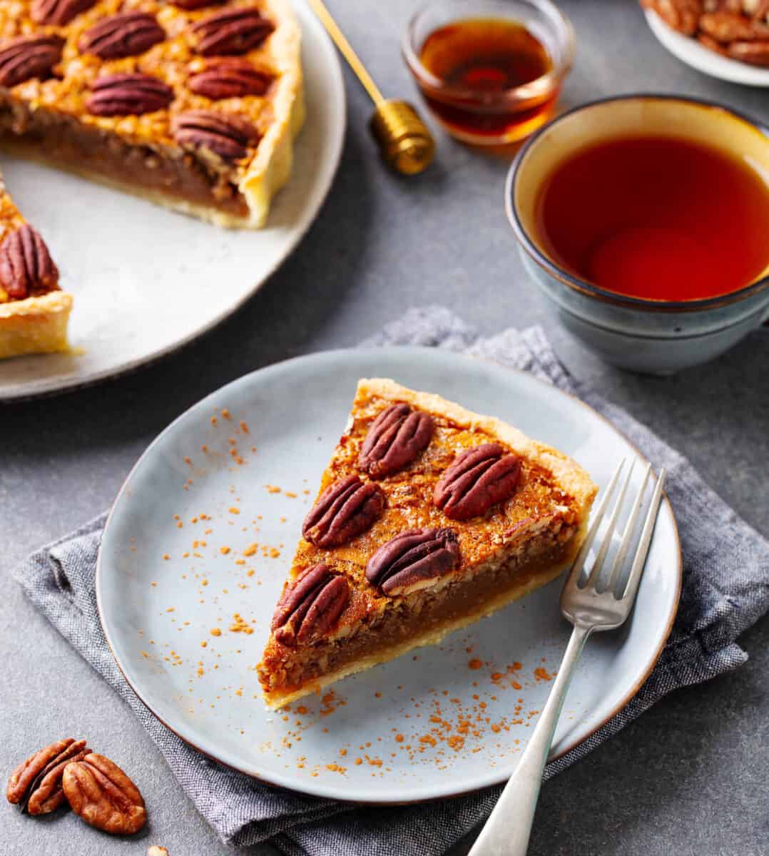 Pecan pie, tart slice on a plate with cup of tea. Grey background.