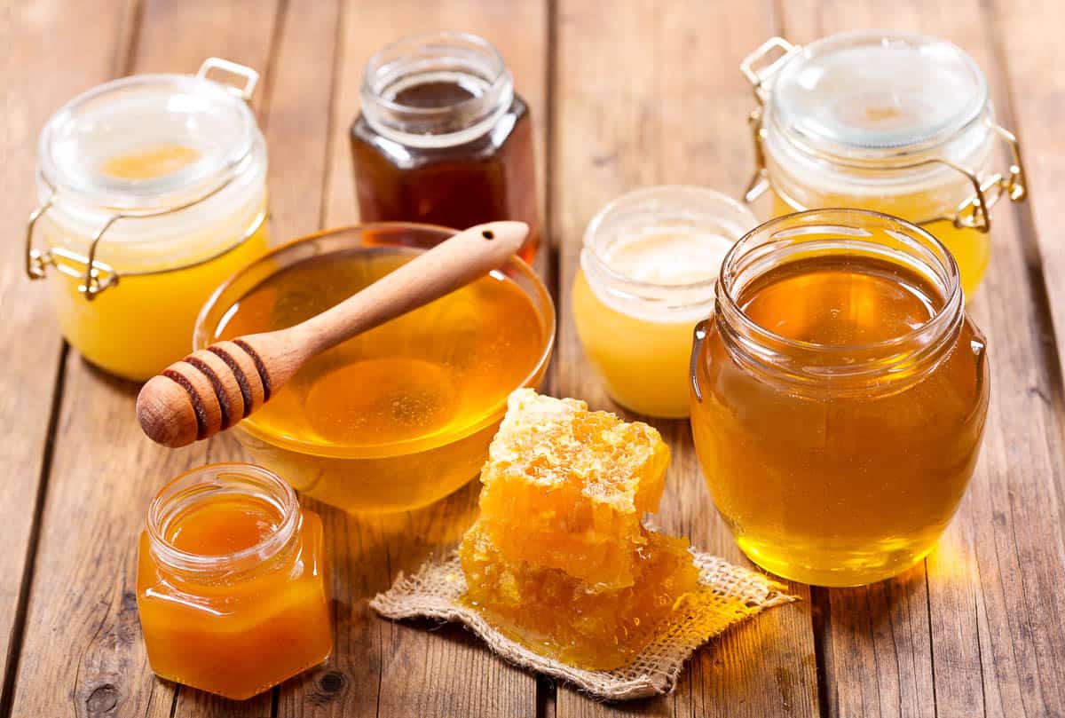 various types of honey in glass jars on a wooden table.