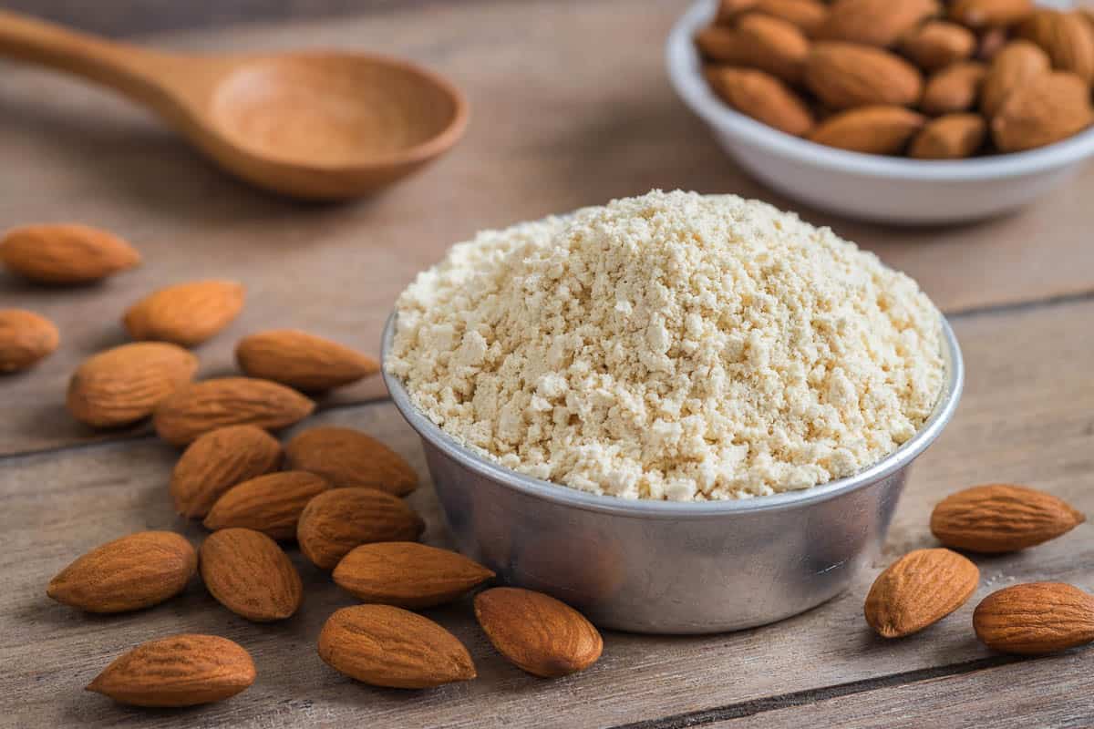 Almond flour in bowl and almonds on wooden table.