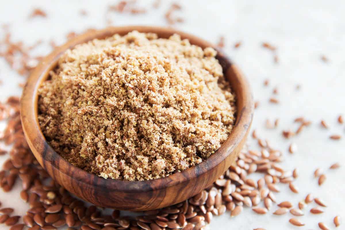 Bowl of crushed flax seeds (ground linseed) on white stone table.