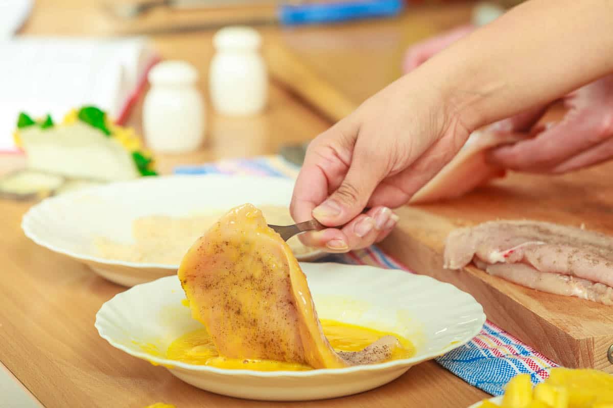 Cooking. Female hand preparing meal of breaded chicken cutlets, in breadcrumbs.