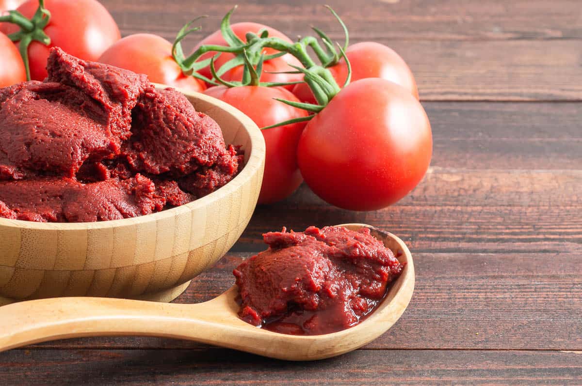 Traditional turkish tomato paste in bowl or spoon with fresh tomatoes on wooden table.