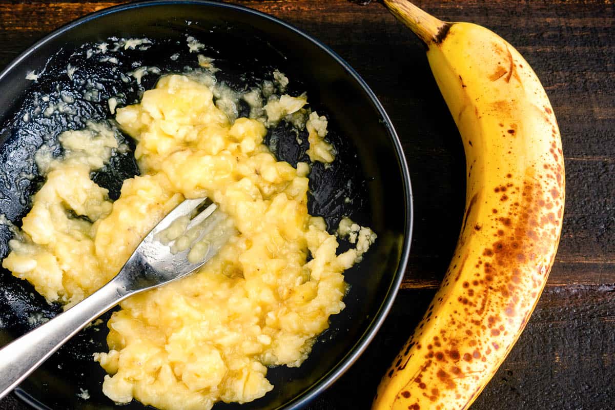 A bowl of mashed banana with a whole ripe banana next to it