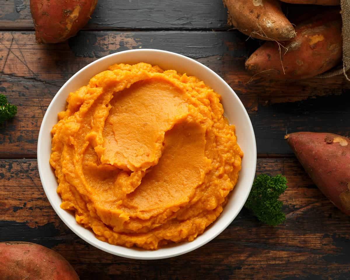 Mashed Sweet Potatoes in white bowl on wooden rustic table.