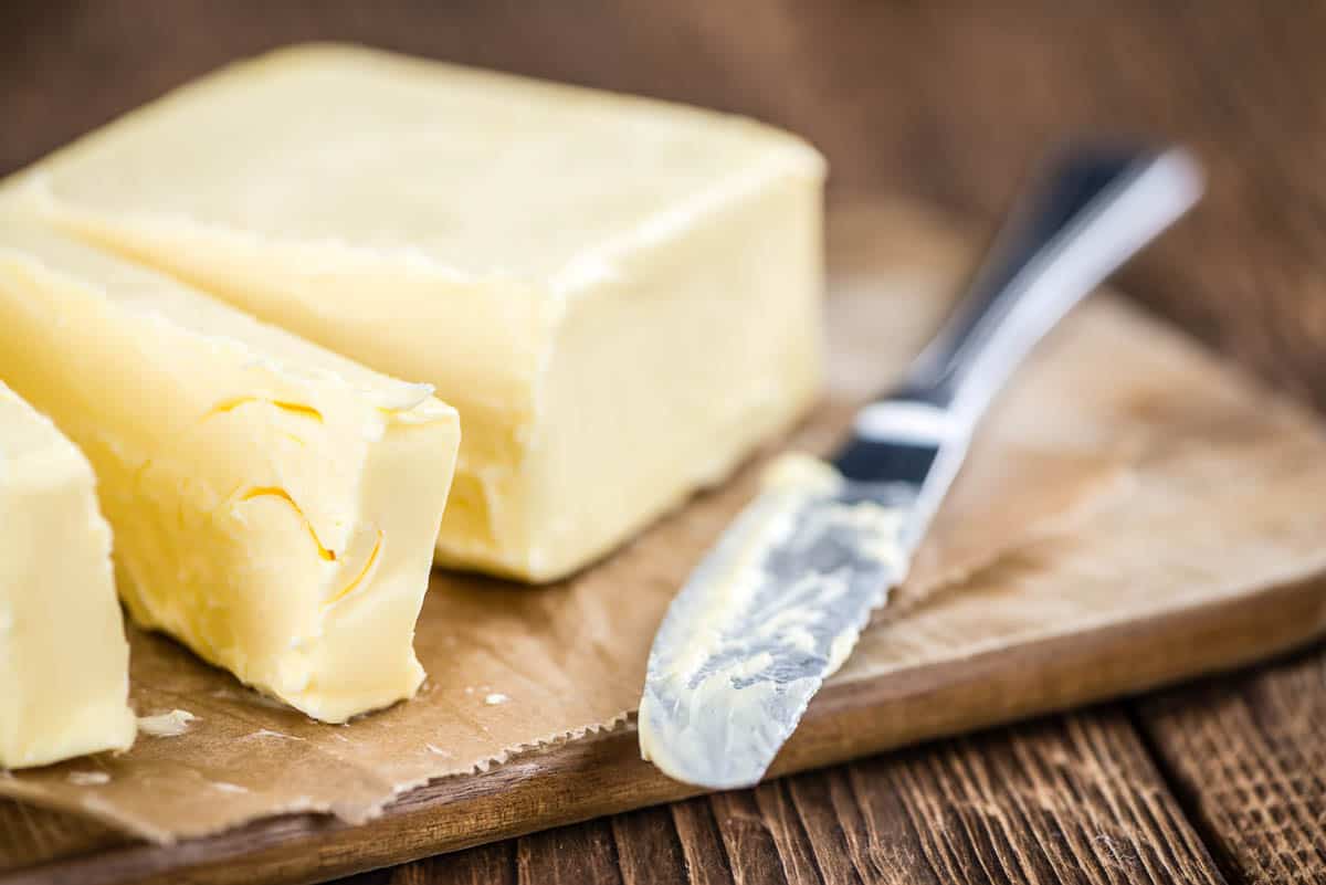 Piece of Butter cut with butter knife on wood cutting board.