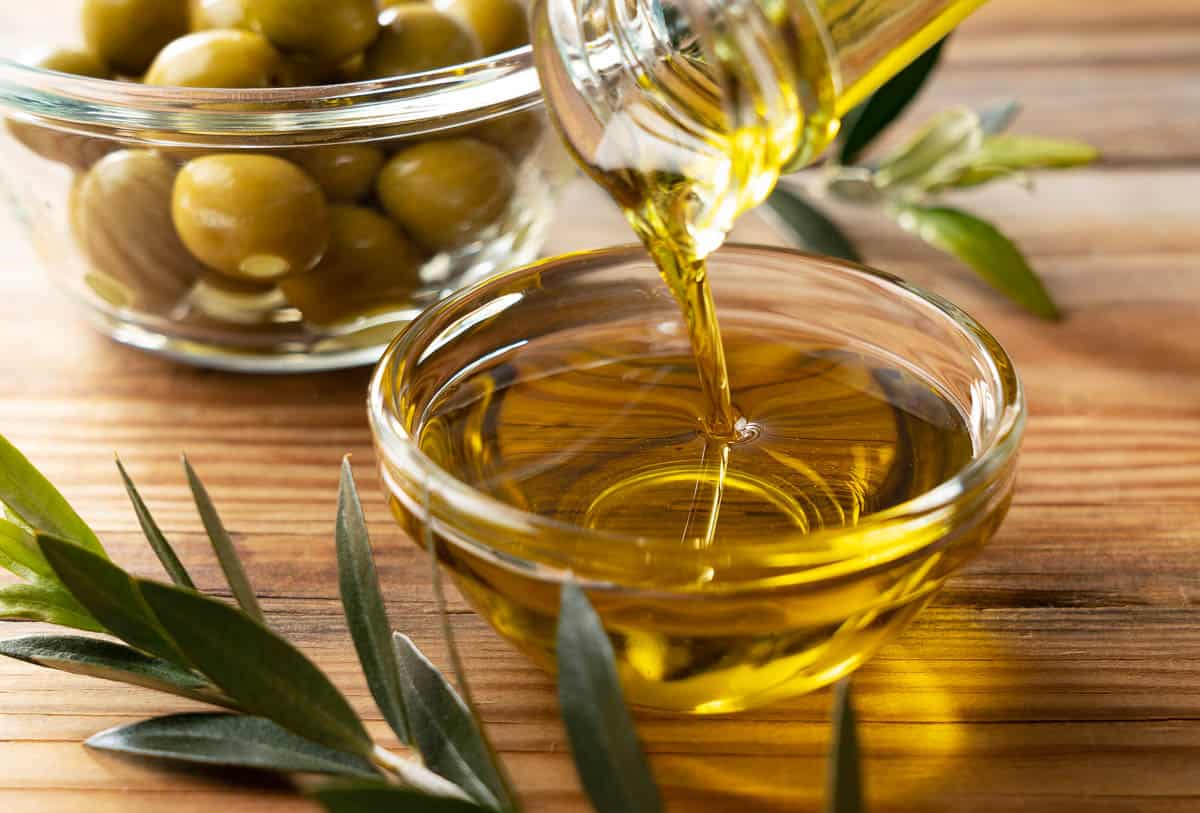 The moment olive oil is poured into a glass bowl set against a wooden background.