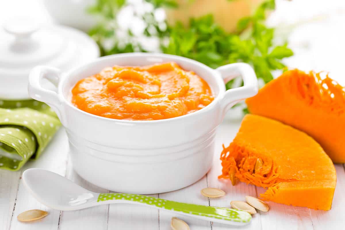 pumpkin puree in white dish next to sliced raw pumpkin.