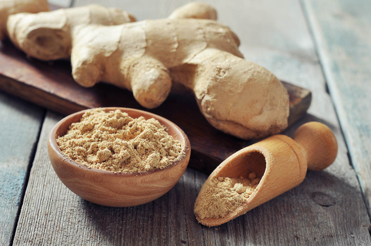 Fresh ginger root and ground ginger spice on wooden background.