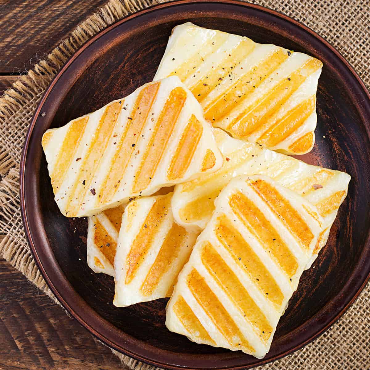 Traditional grilled halloumi cheese on plate on wooden background.