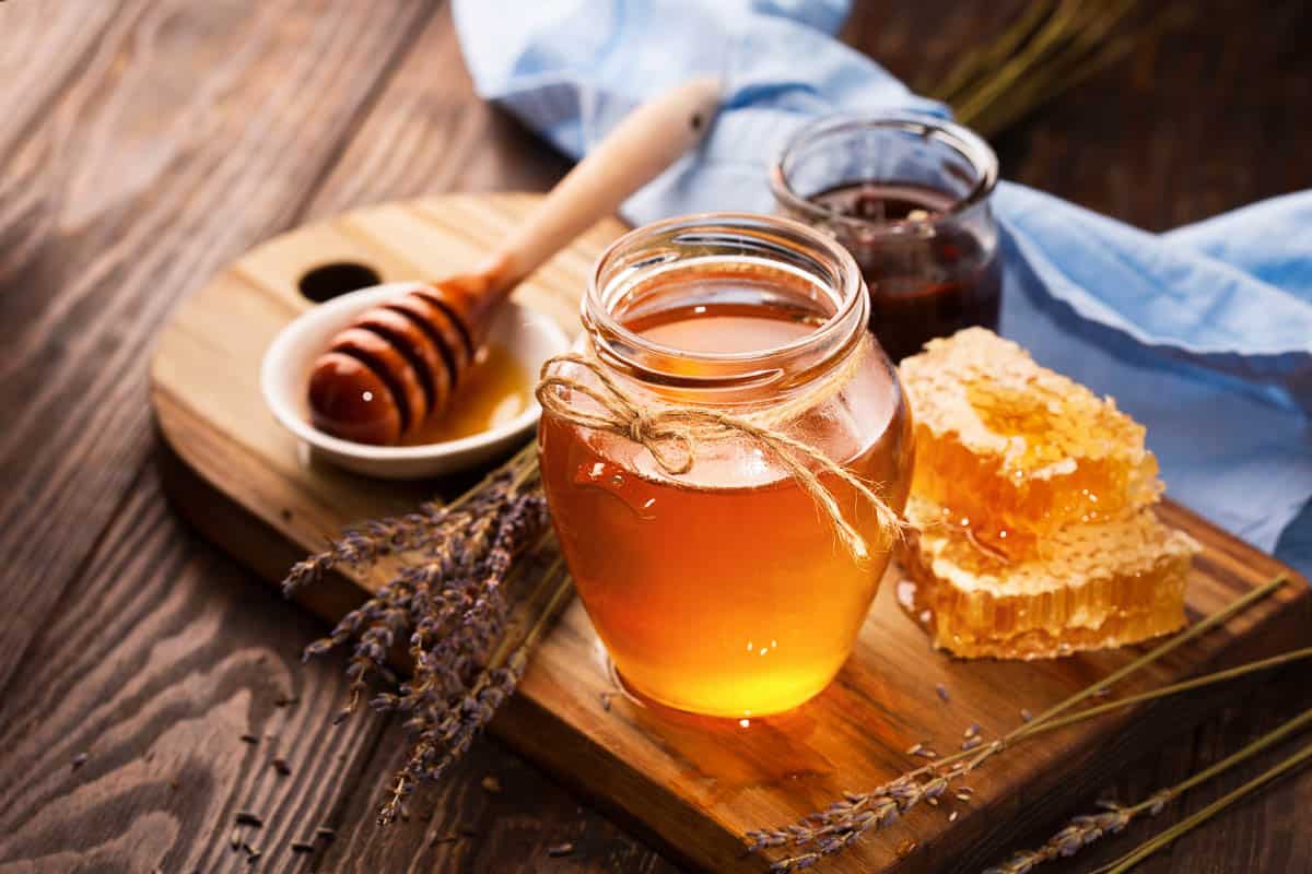 Jar of liquid honey with honeycomb inside and bunch of dry lavender over old wooden table.