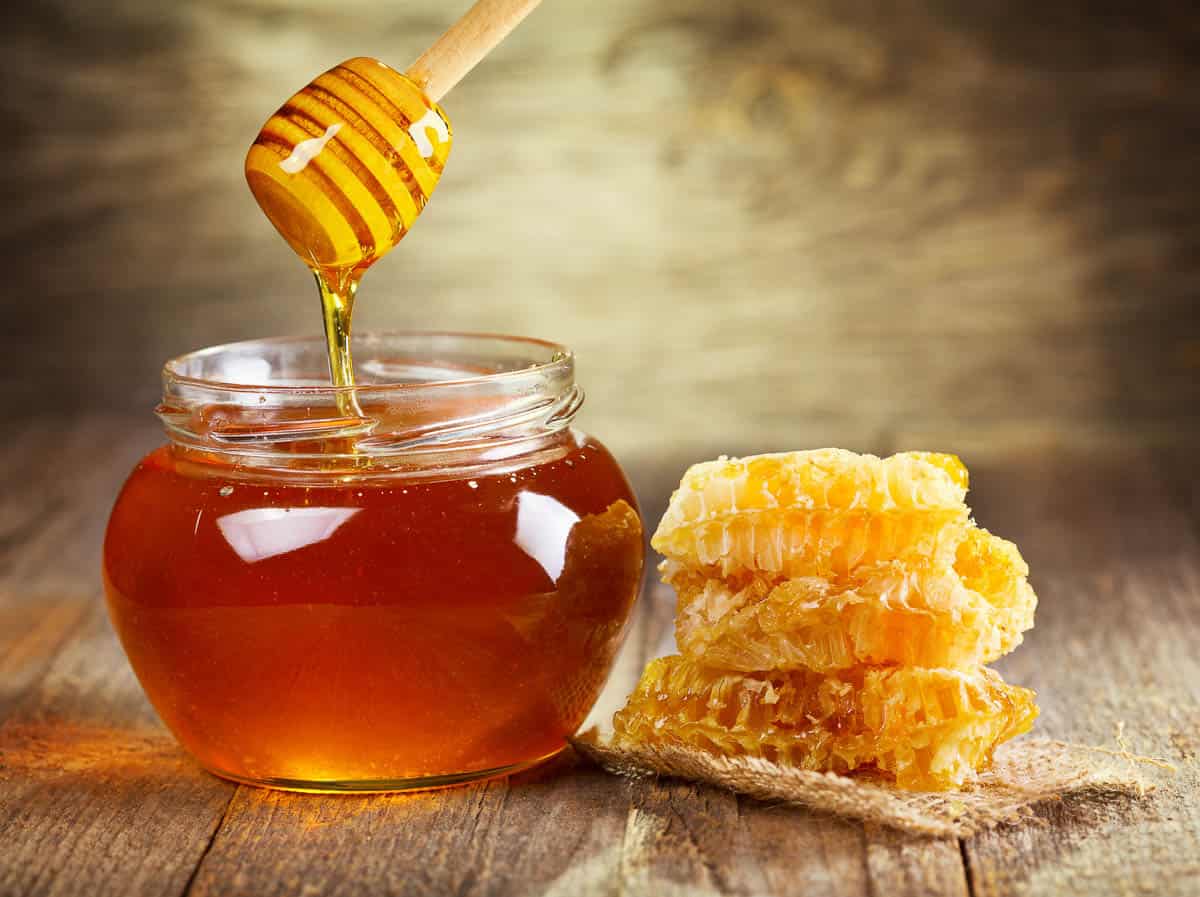 jar of honey with honeycomb on wooden table.