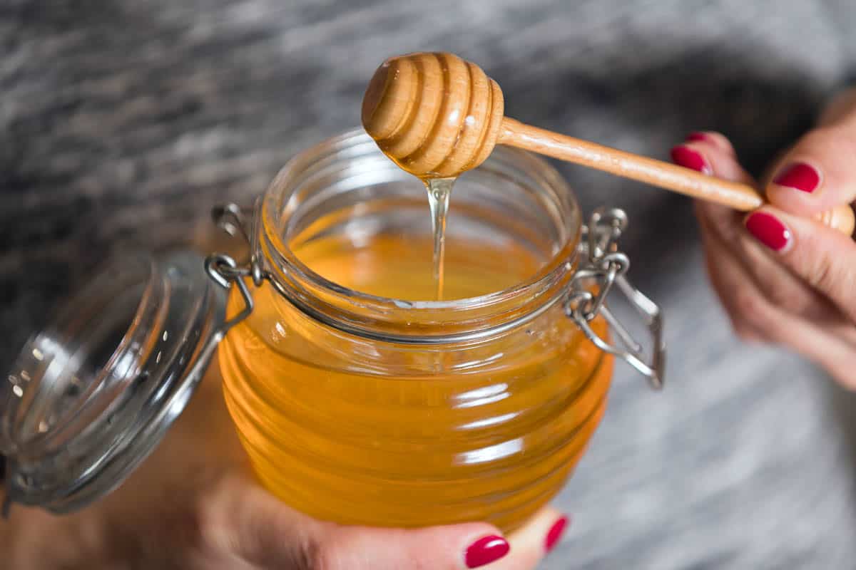 Woman hand holding glass jar of honey.