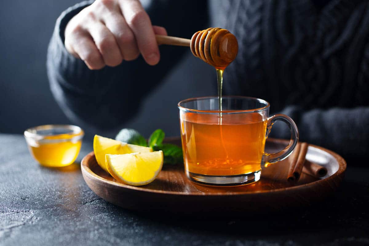 Cup of tea with pouring honey and lemon.