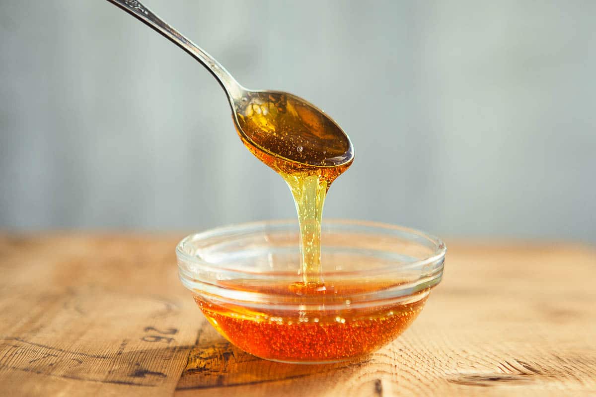 Honey dripping from spoon in the cup in golden sunlight.