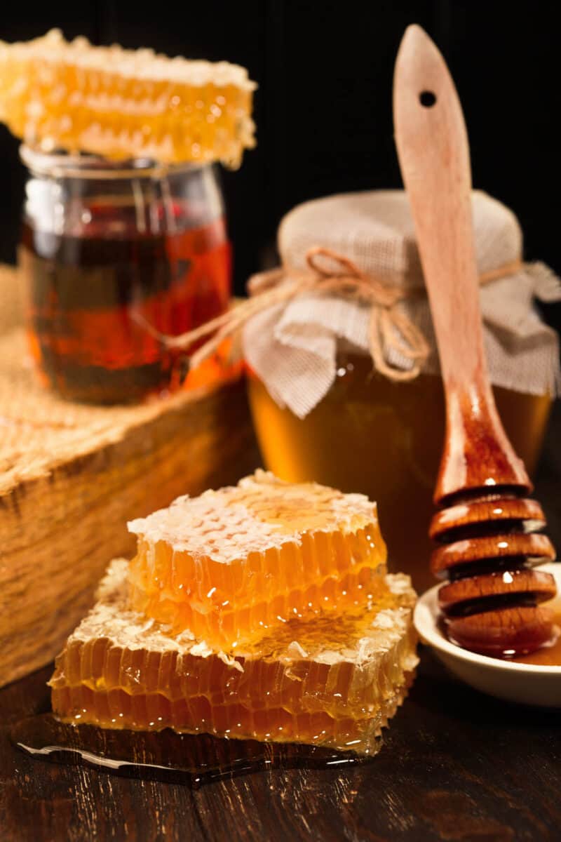 Jar of liquid honey with honeycomb inside over old wooden background.