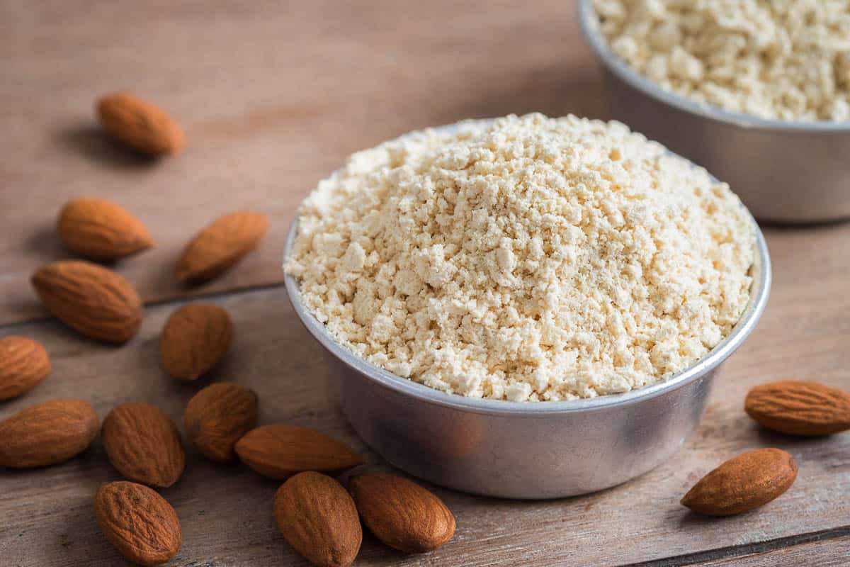 Almond flour in bowl and almonds on wooden table.