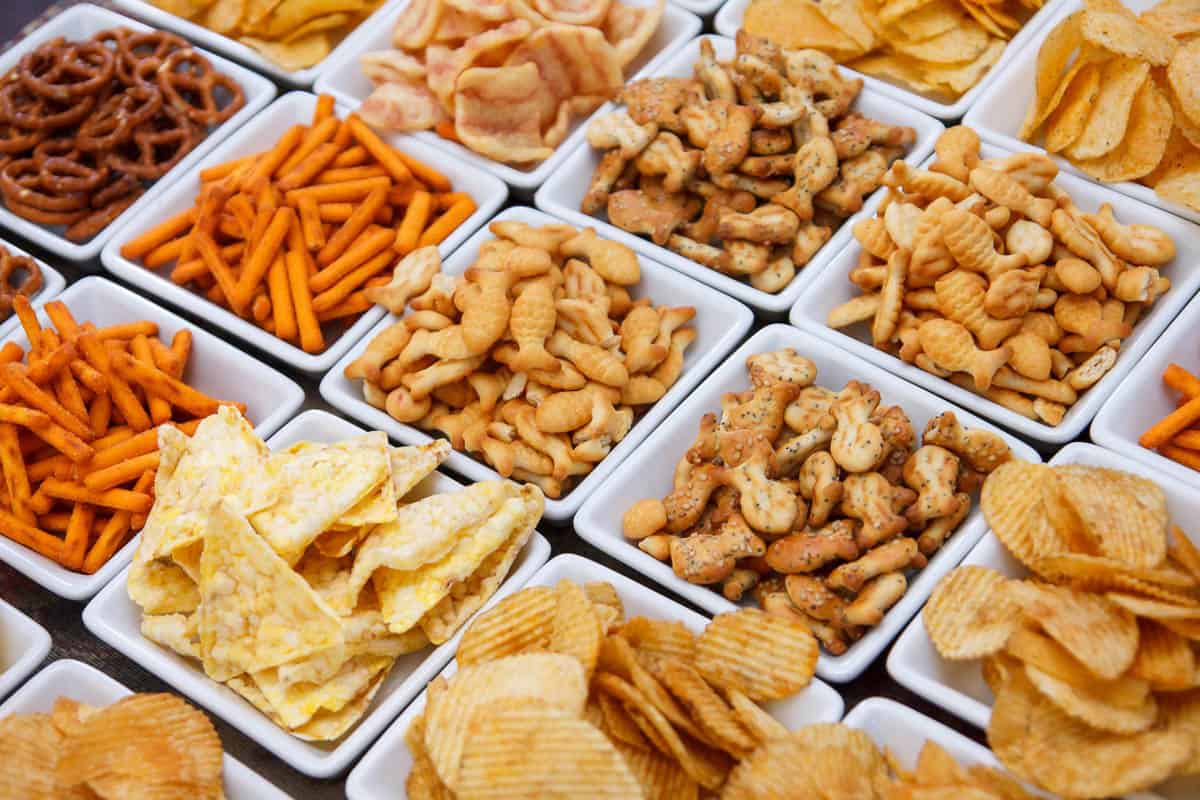 Many types of savory snacks and chips in white dishes.
