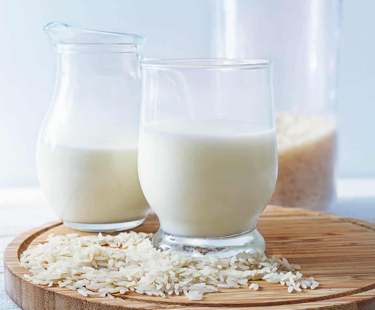 Vegan rice milk in glass with uncooked rice.