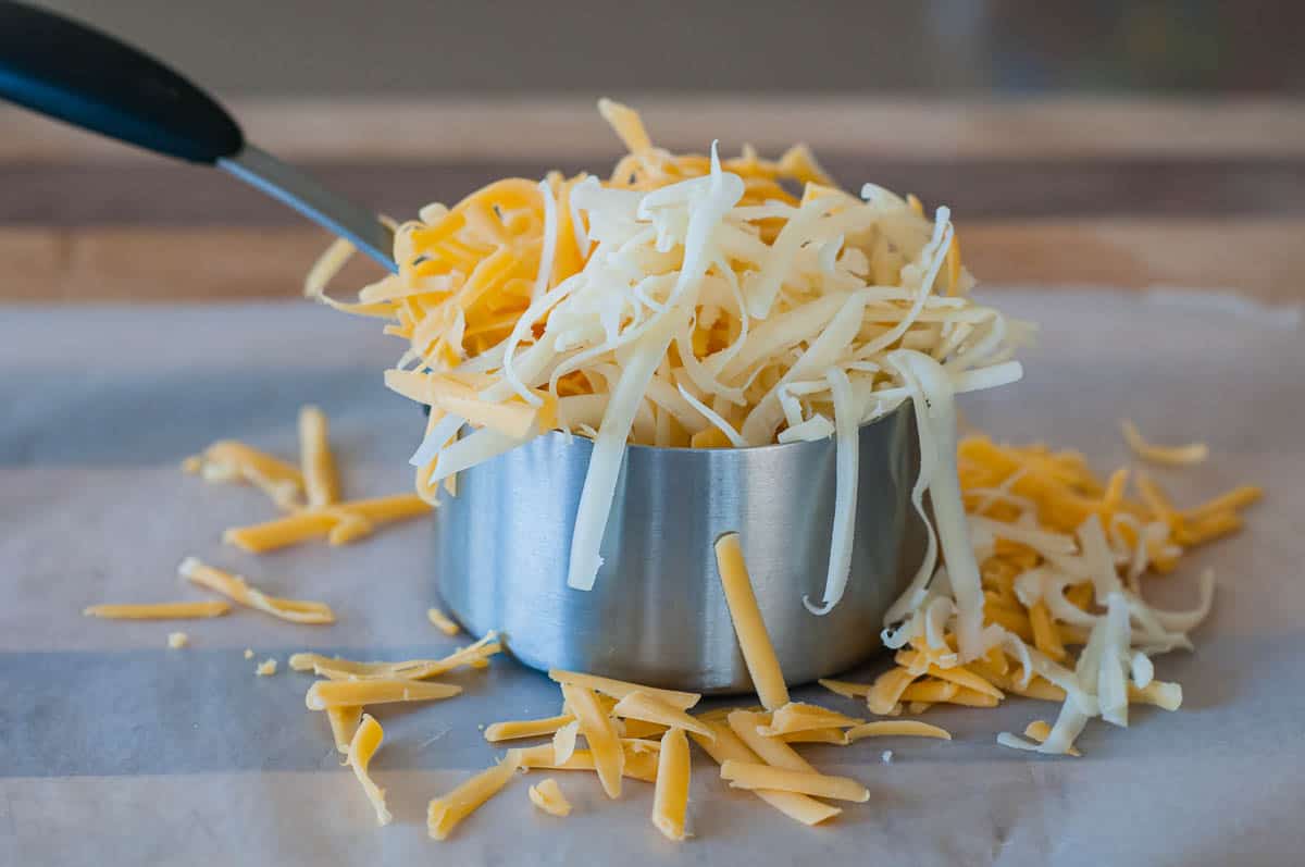Close-up of overflowing measuring cup of grated orange and white cheese.