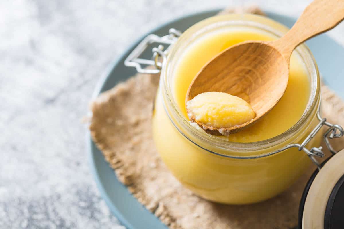 Ghee or clarified butter in jar and wooden spoon.