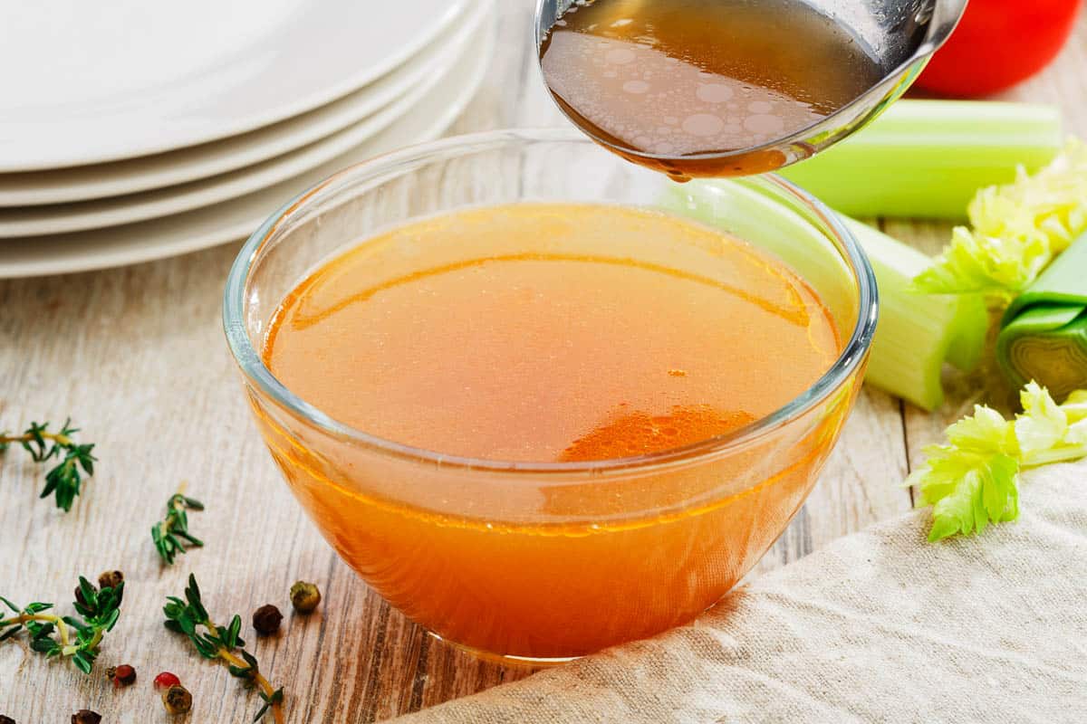 A clear bowl of chicken broth with herbs and celery