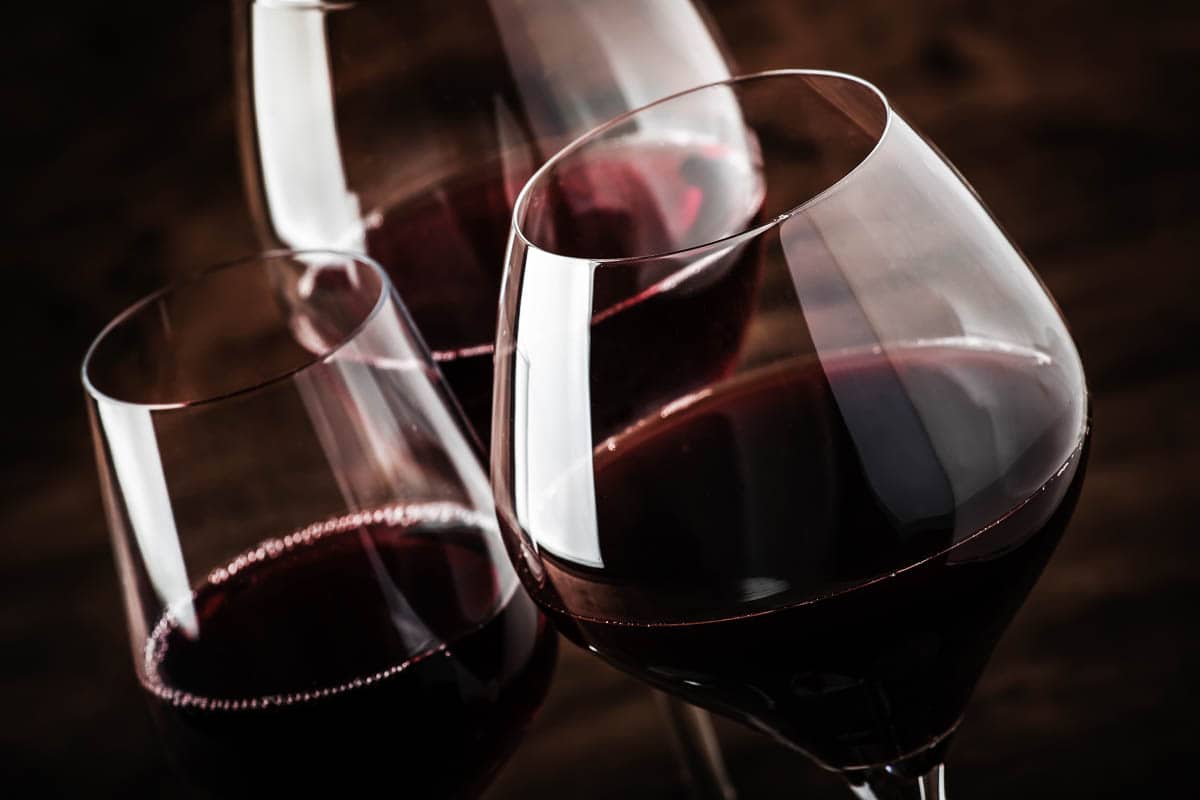 Dry, semi-dry, sweet red wines in special wine glasses on old wooden table background.