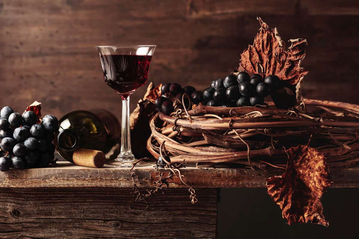 Crystal glass and bottle of port red wine with grapes on an old wooden table.