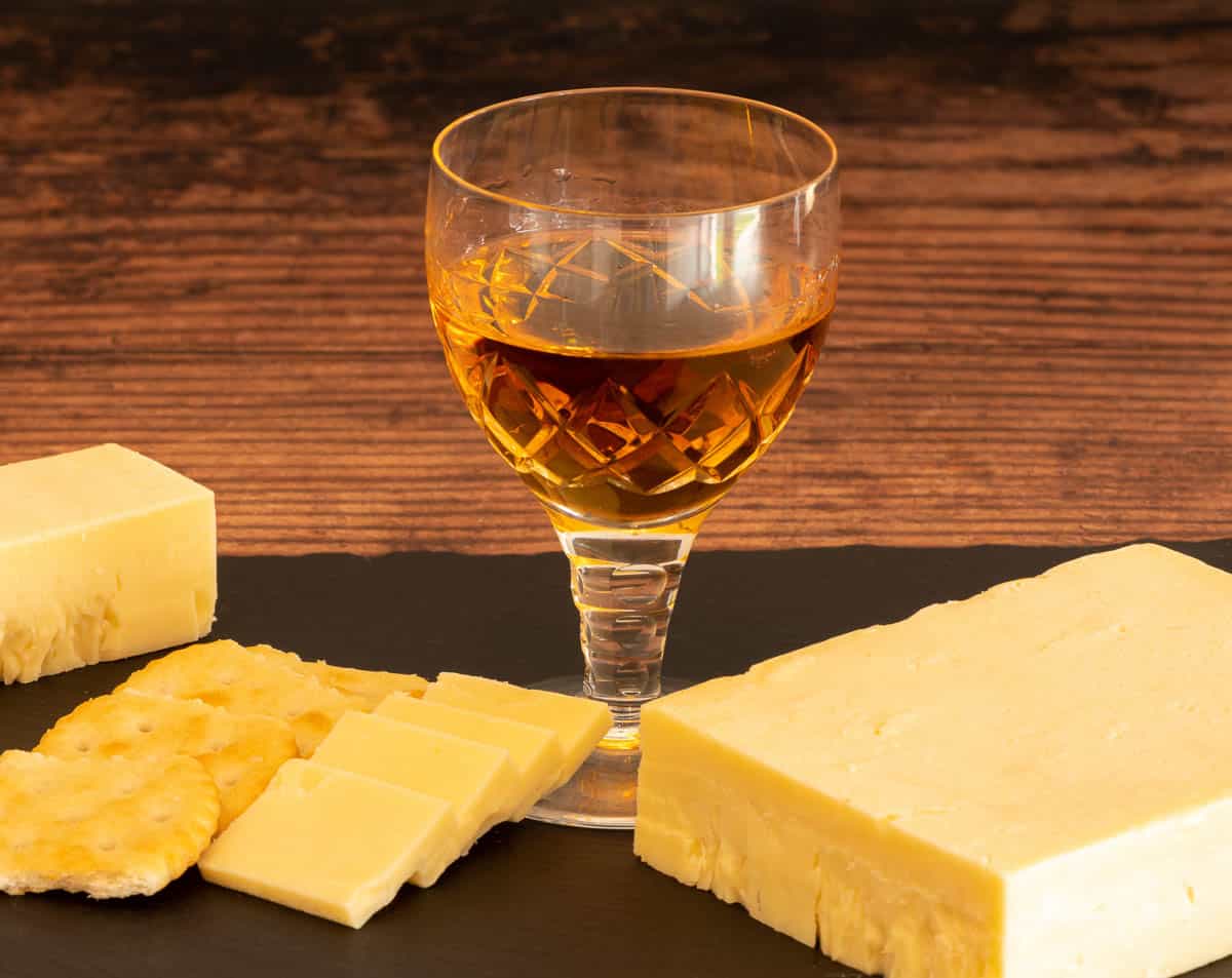 Block of cheese with crackers sliced apple and a glass of sherry on the side.