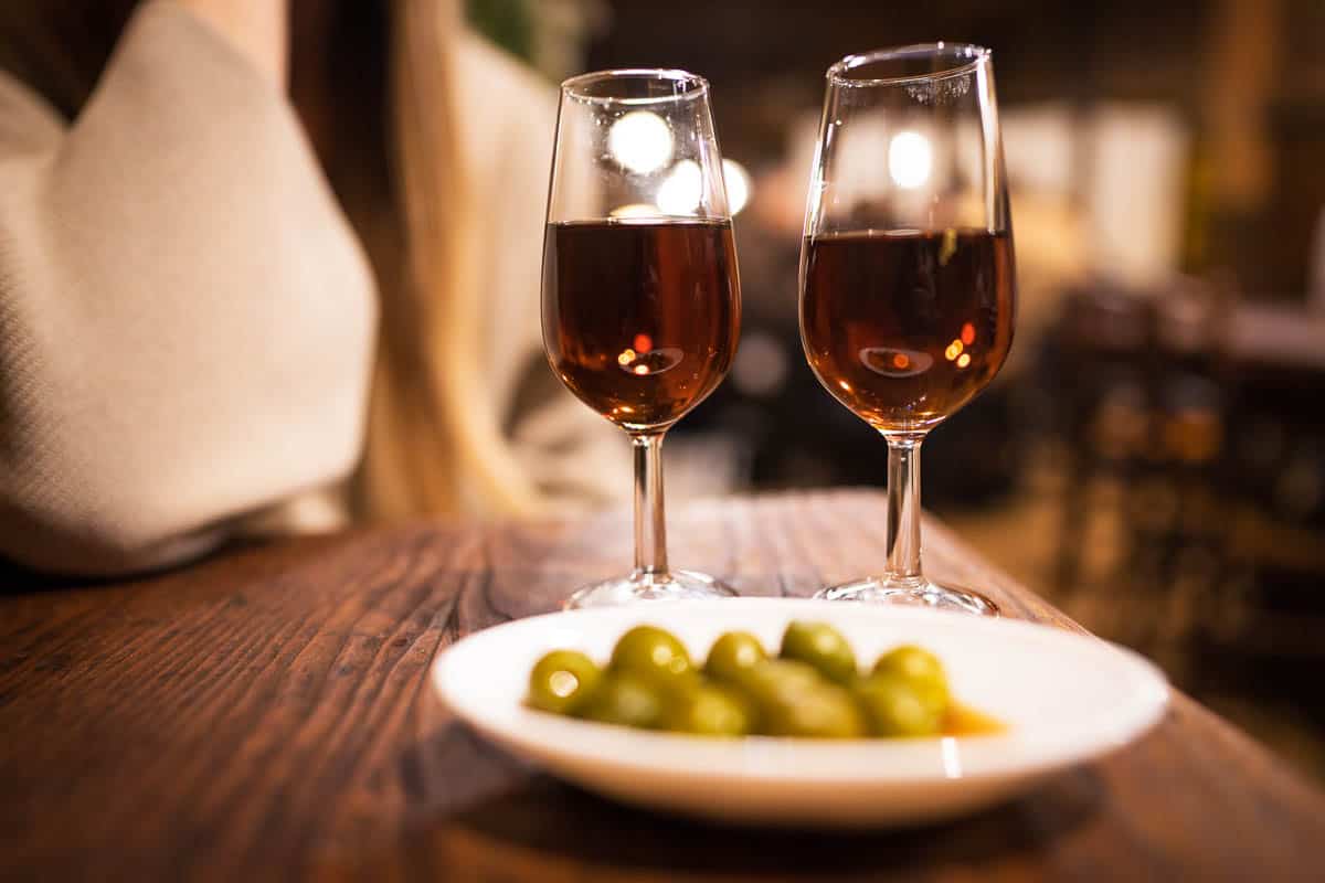 This image capture shows vermouth and olive tapas for two at a rustic, classic wine bar in Spain.