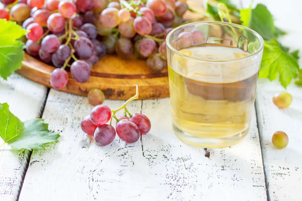 A glass of sweet grape juice, freshly squeezed, a bunch of fresh grapes on a white wooden table.