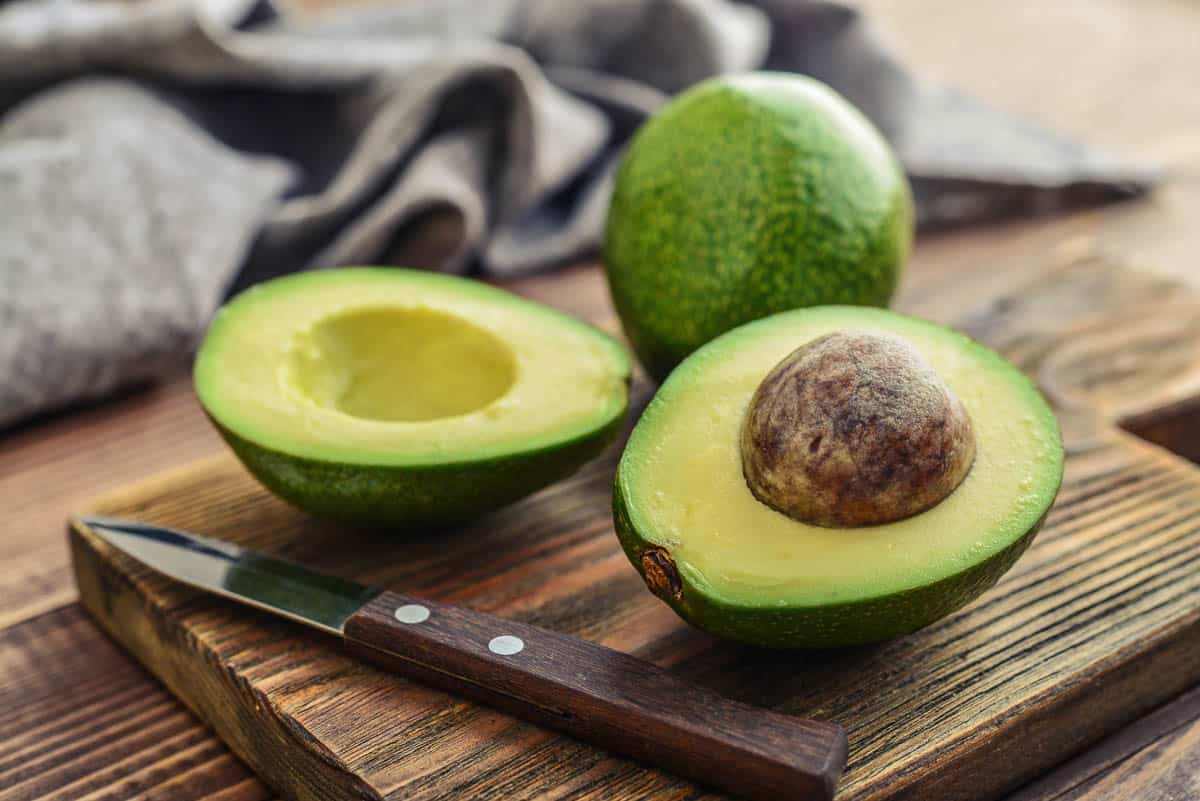 Fresh avocado on cutting board over wooden background.