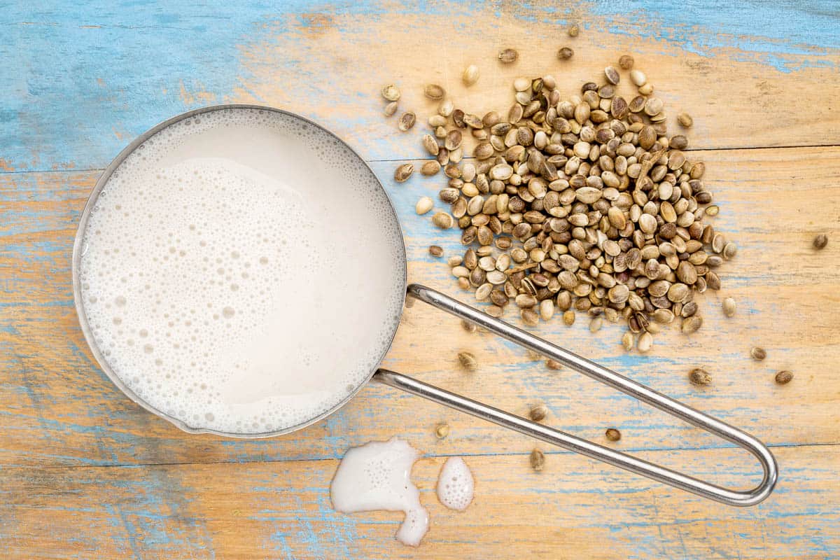 hemp milk in measuring cup with seeds against wooden background.