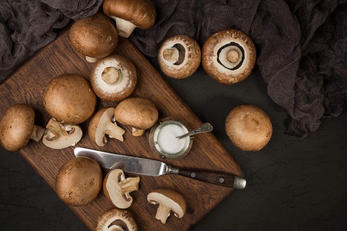 Fresh champignon mushrooms on a cutting board and on a black background.