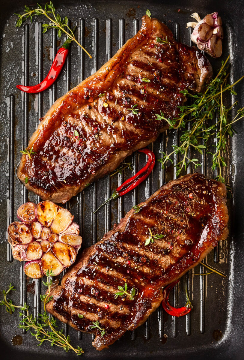 Grilled striploin steak with spices and herbs on grill iron pan.