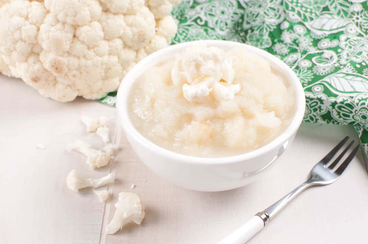 pureed cauliflower in white dish in front of head of cauliflower.