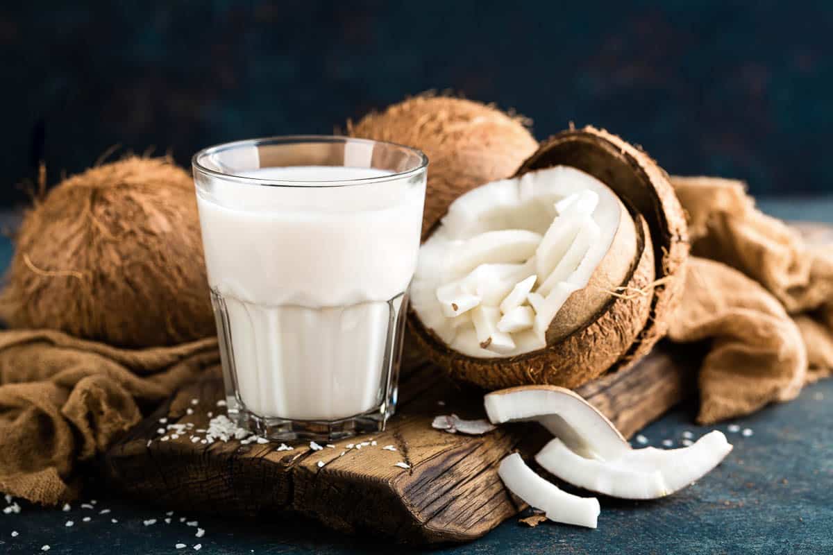 Fresh coconut milk in glass with whole coconuts on side.