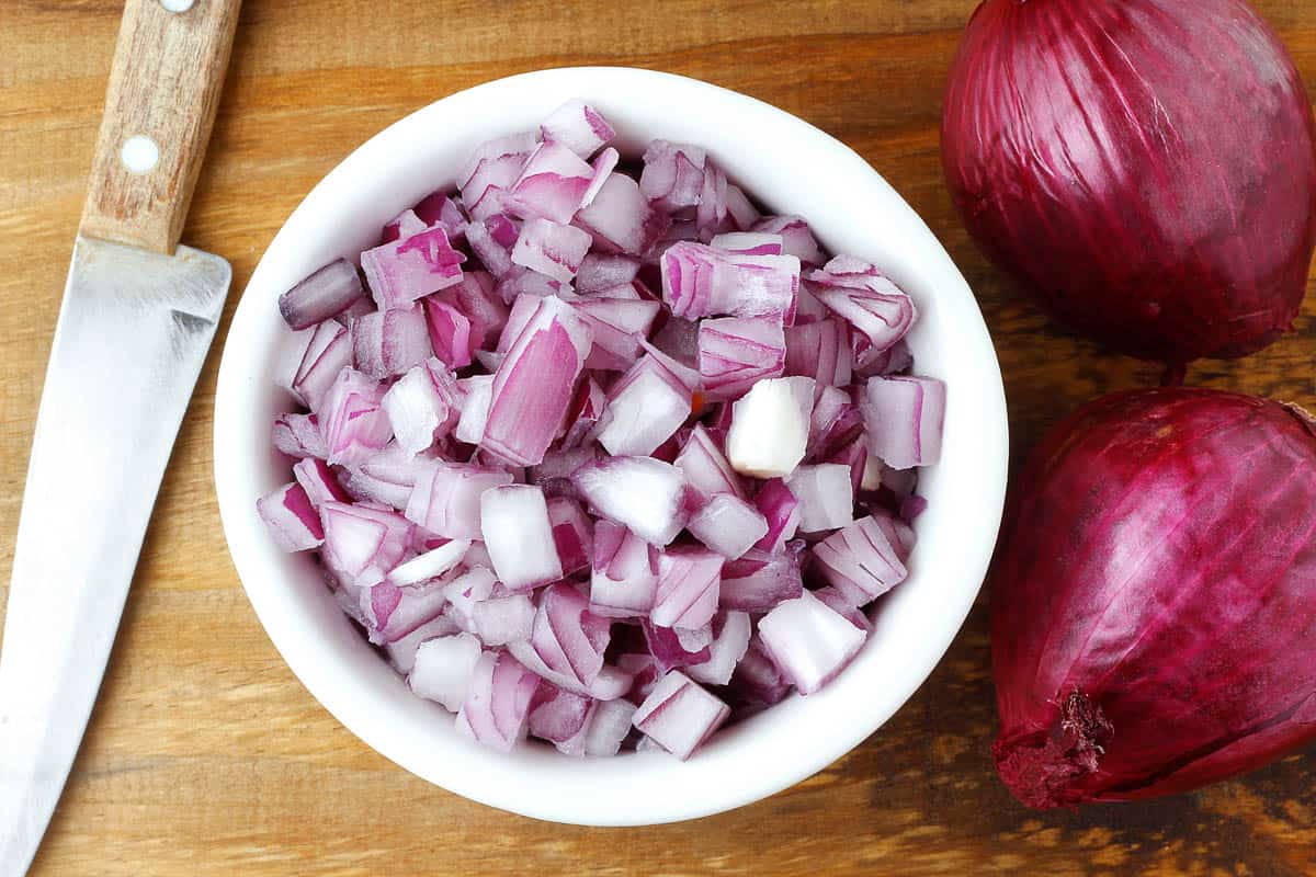 chopped raw red onion in white ceramic bowl.