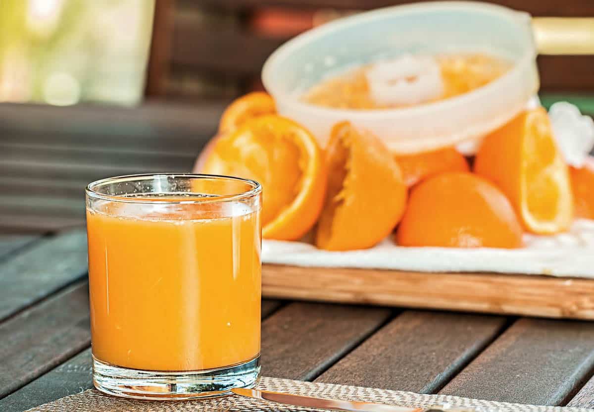 glass of orange juice with oranges and juicer in background