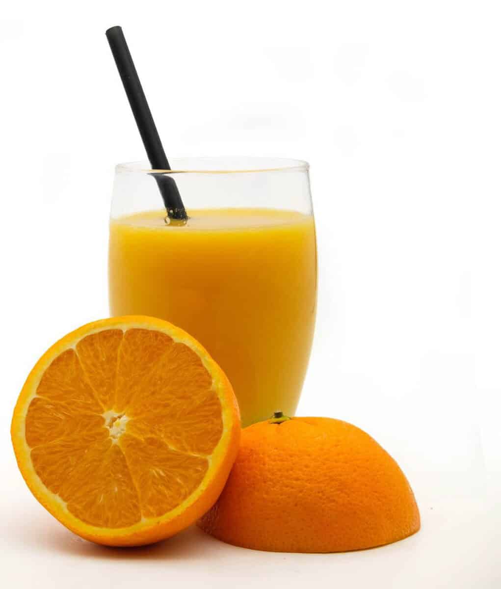 glass of orange juice with orange cut in half on white background