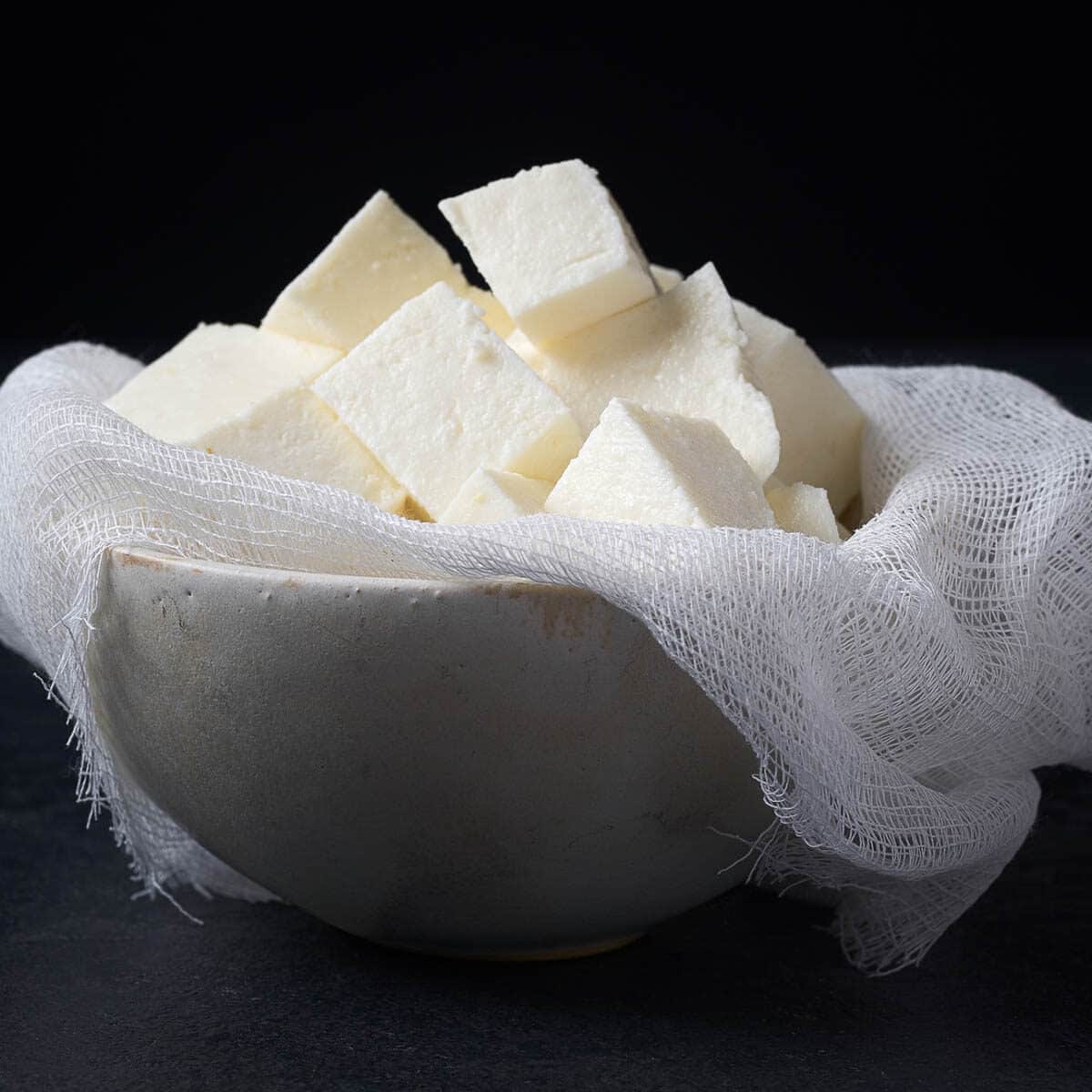 TraditiTraditional Indian homemade fresh paneer cheese. onal indian cheese paneer. Vegetarian homemade soft cheese in cheesecloth on dark background.